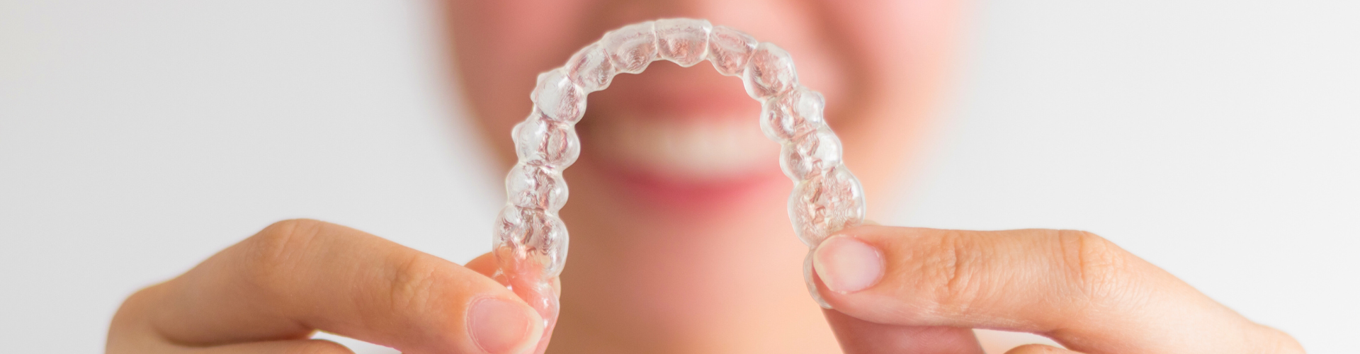 Smiling woman holding clear aligner.